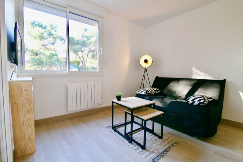 Living room with sofa bed and a window onto the trees, “Tamaris, entre pinède et mer” apartment