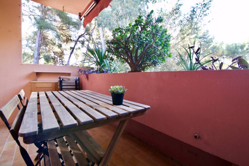 Terrace with a wooden table and chairs under the pines, “Tamaris, entre pinède et mer” apartment